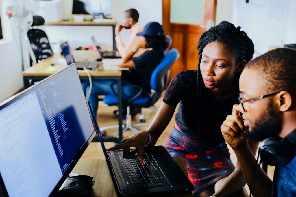 A female person explaining something to a male person while pointing on laptop screen